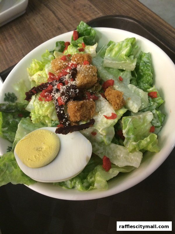 A close-up of a Caesar salad with croutons, egg, and dried fruit.