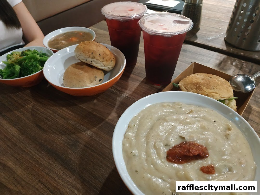 A table laden with various dishes including soup, bread rolls, broccoli, drinks, and a sandwich.