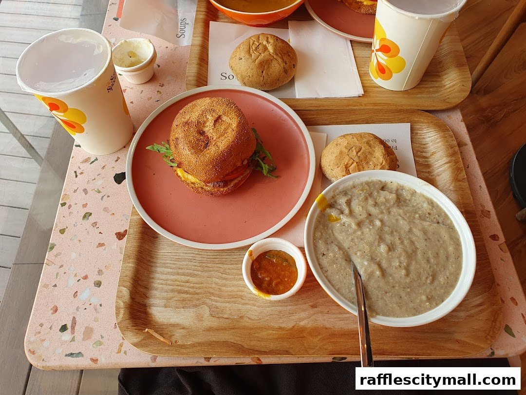 A table setting with a burger, soup, bread rolls, and drinks from The Soup Spoon.