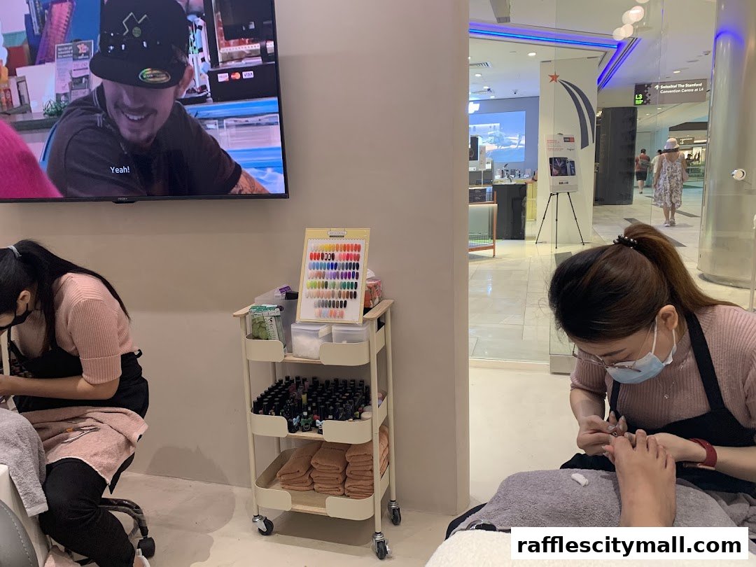 Nail technicians working on clients' feet and hands, with a nail color display and TV.
