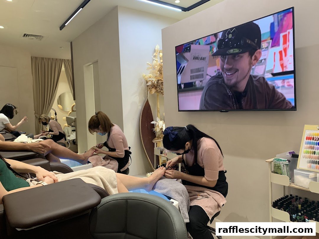Nail technicians providing pedicures to clients in a modern salon with a TV screen.