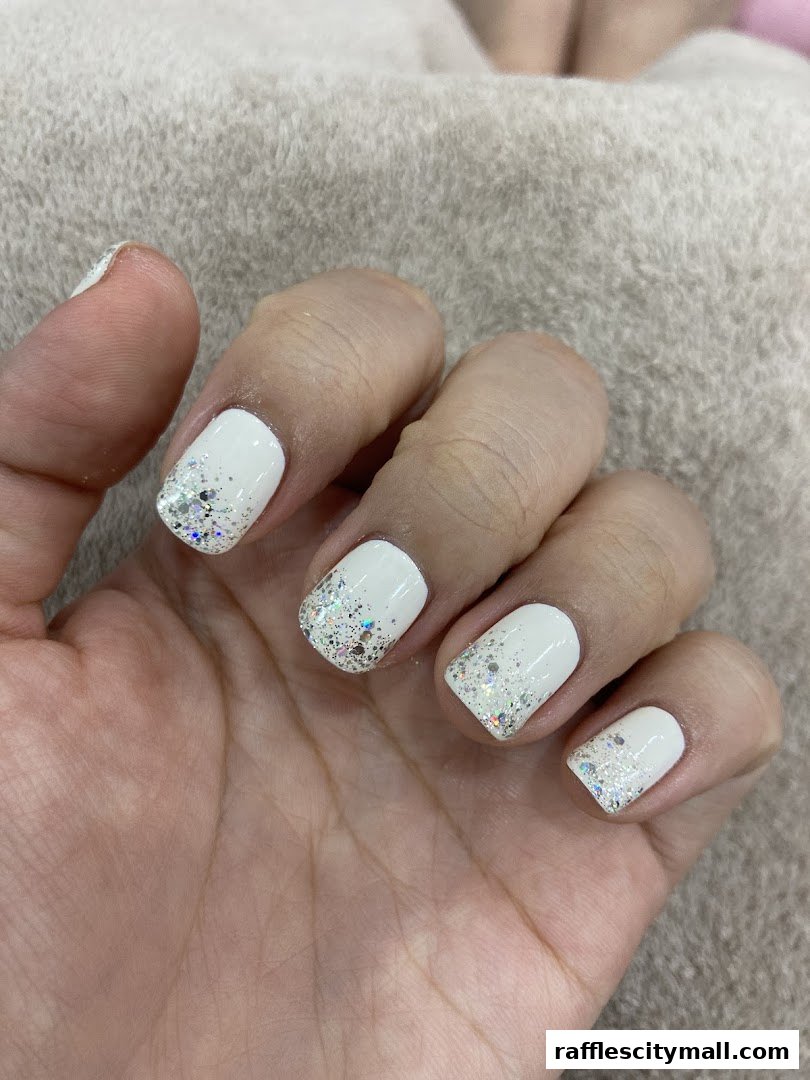 A close-up of a hand with white nails adorned with glitter accents.