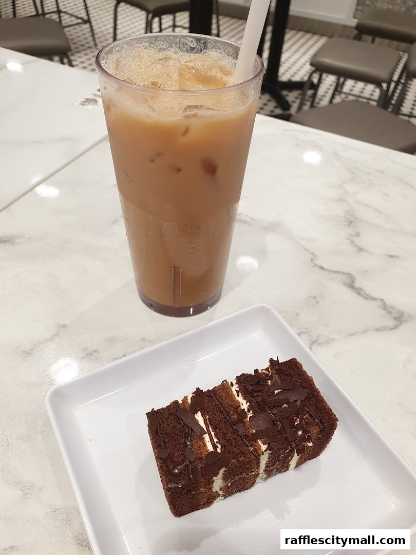 A slice of chocolate cake and a tall glass of iced tea on a marble table.