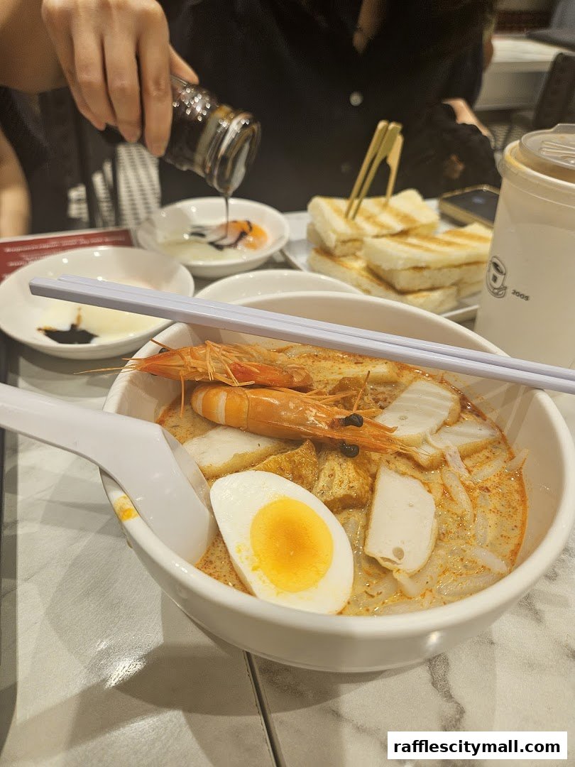 A bowl of Laksa with prawns and egg, served with toast and coffee.