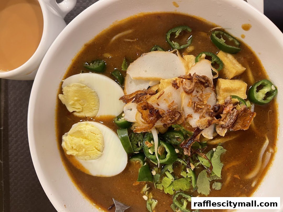 A close-up of a bowl of noodles with egg, fish cake, and chili, served with a cup of tea.
