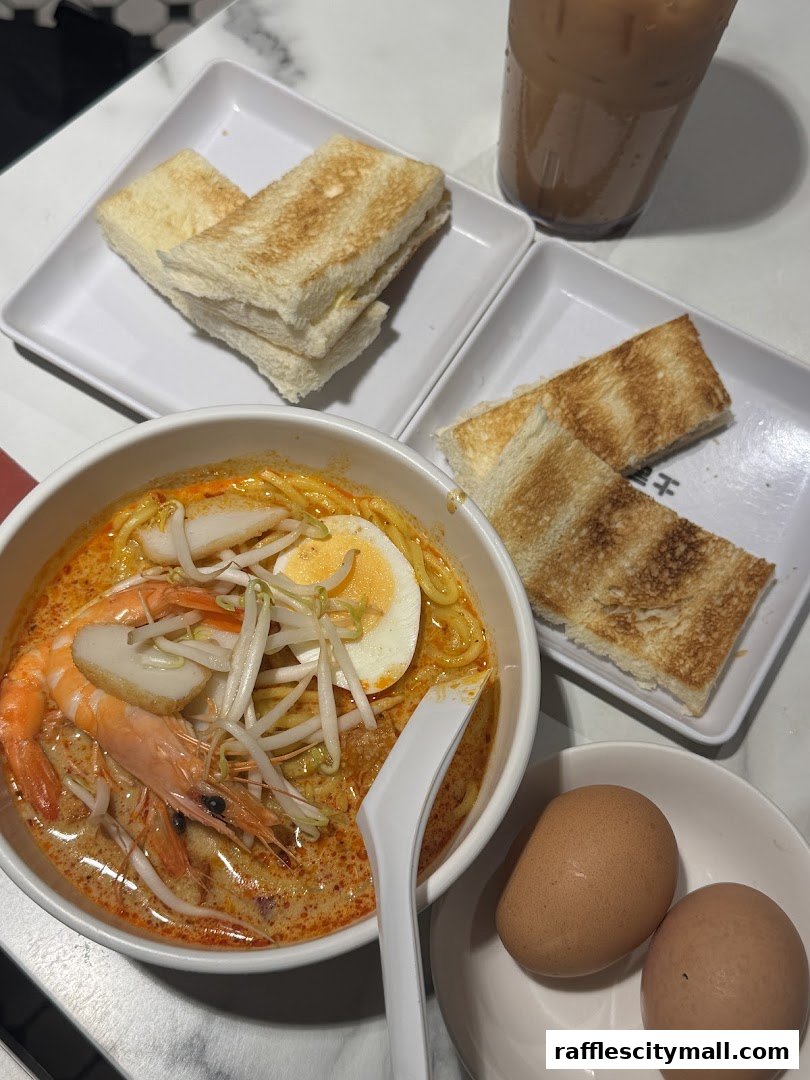 A bowl of Laksa with toast, eggs, and a drink.