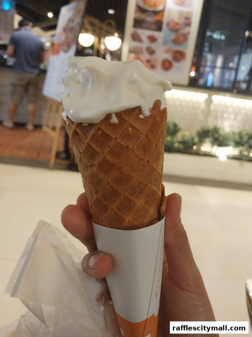 A hand holds a melting ice cream cone with a waffle cone.