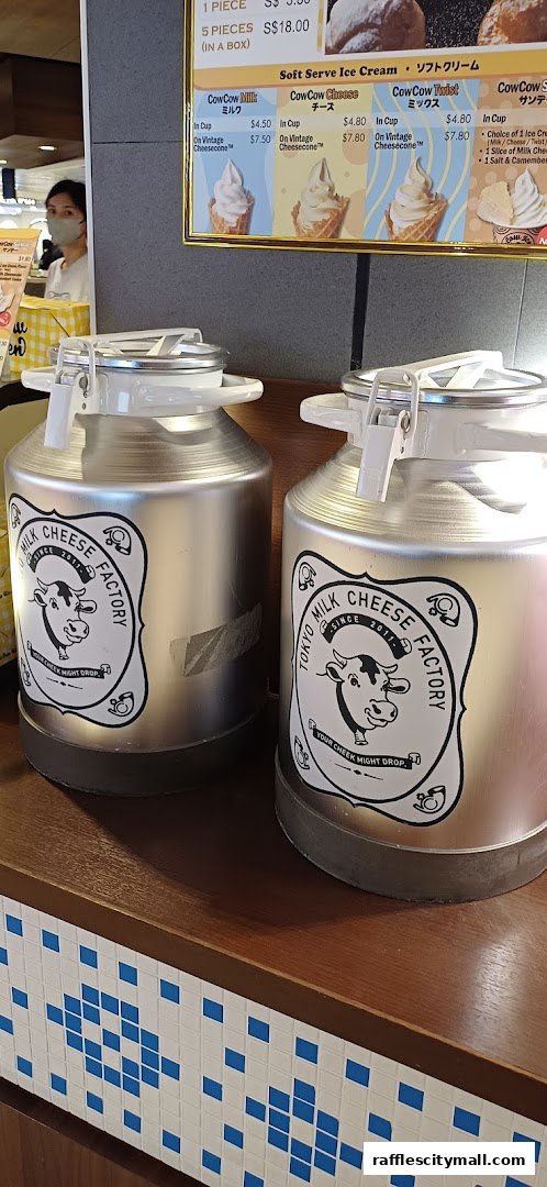 Two large silver milk cans with Tokyo Milk Cheese Factory branding are displayed on a wooden counter.