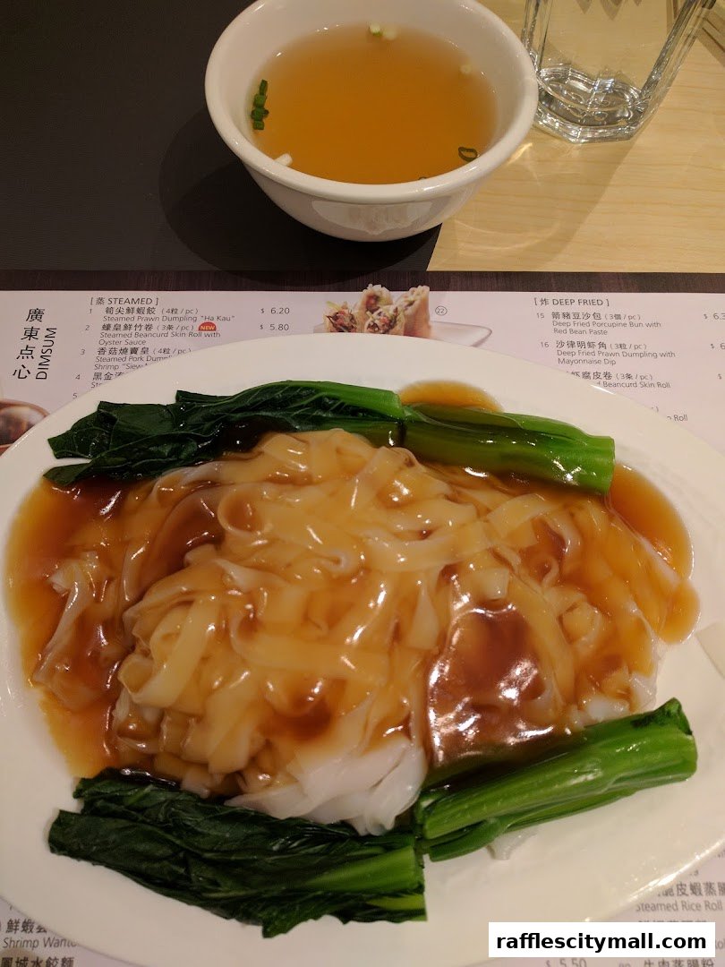 A plate of steamed rice noodle rolls with vegetables and a bowl of soup.