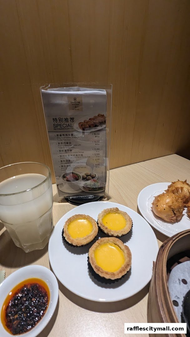 A table setting with dim sum, egg tarts, chili sauce, and a drink.