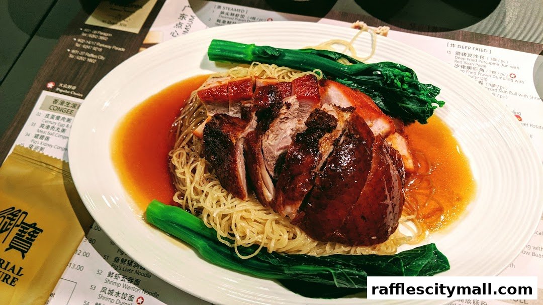 A plate of roasted duck and char siu with noodles and greens, with a menu in the background.