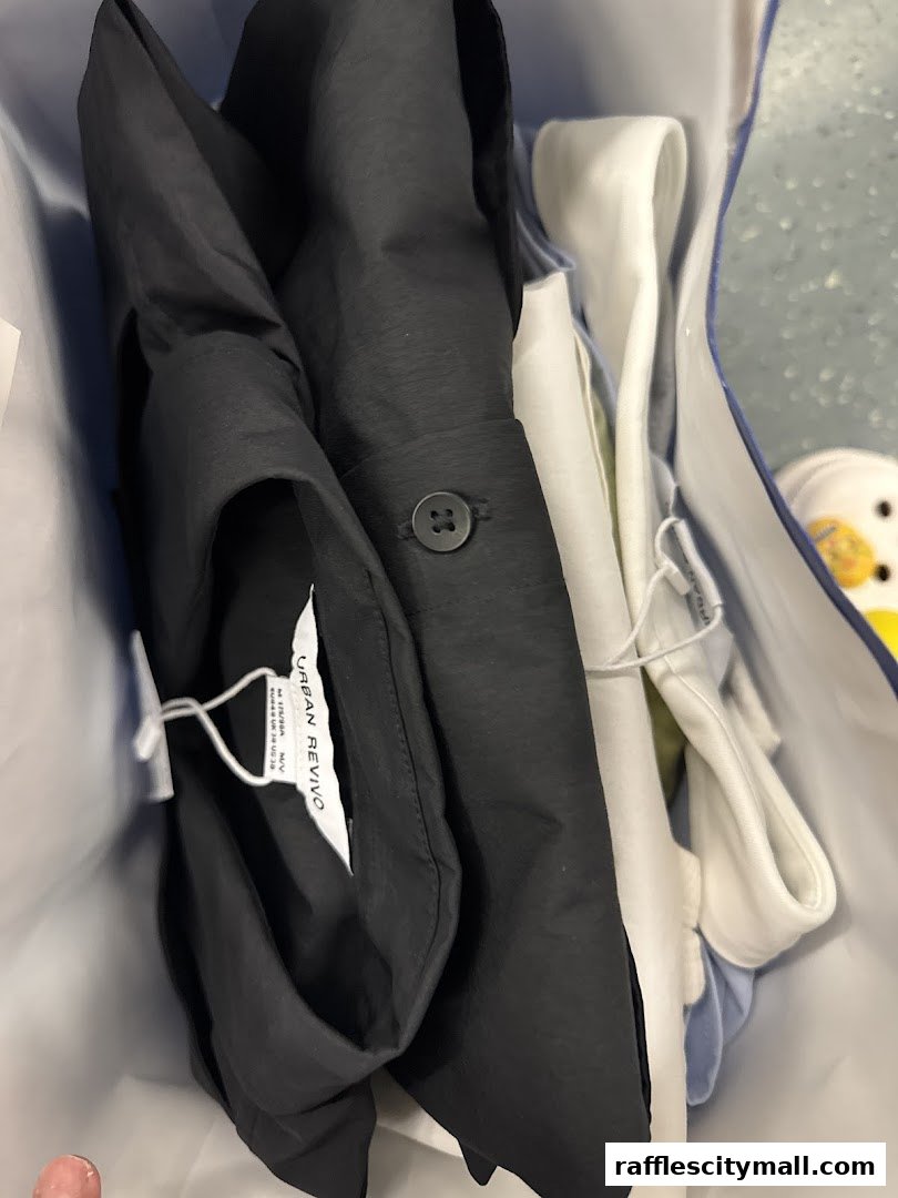 A shopping bag filled with folded clothes, including a black shirt with a button.