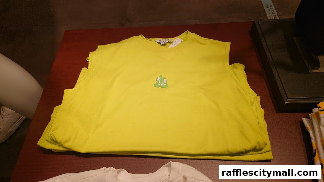 A stack of bright yellow sleeveless shirts with a small green pixelated character embroidered on the chest.