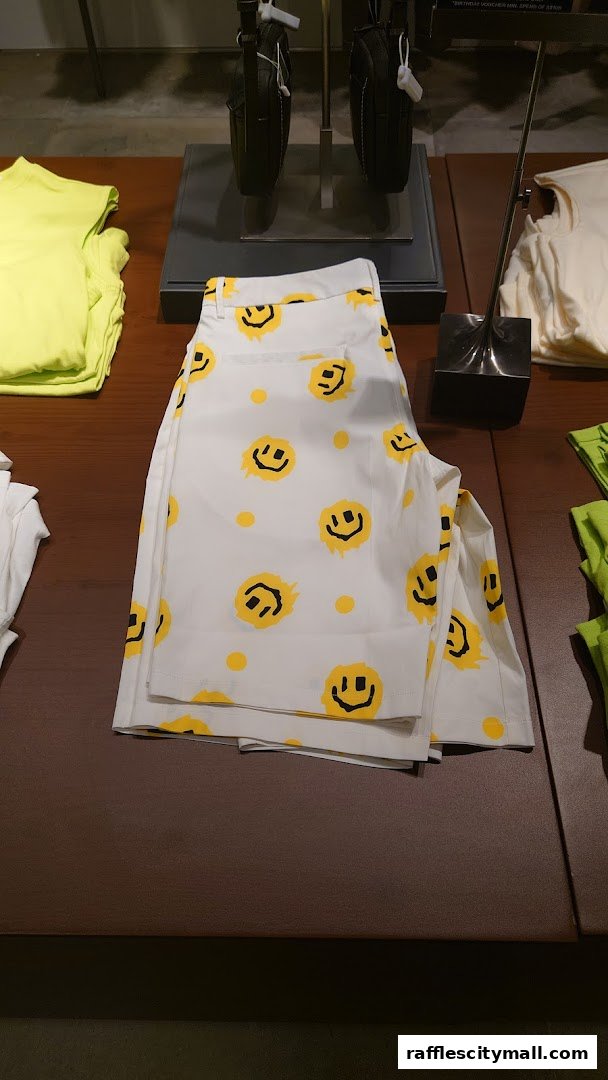 Folded white pants with a yellow smiley face pattern displayed on a wooden table.