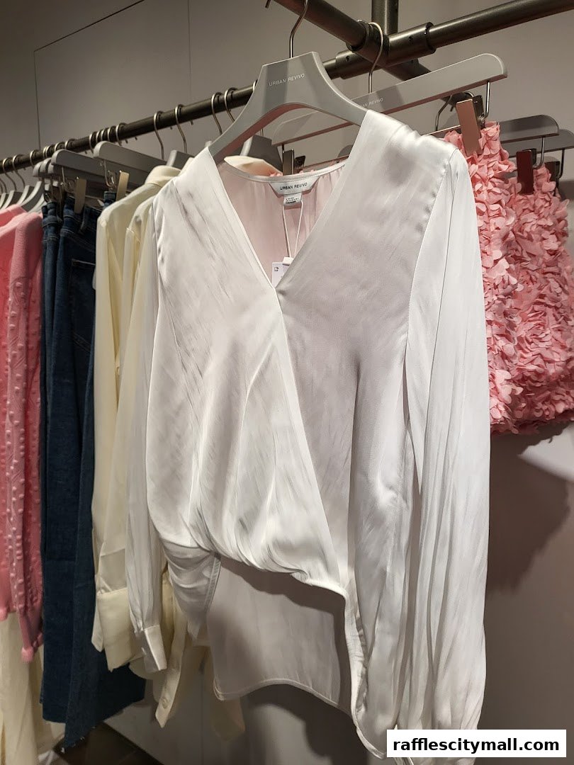 A white satin blouse with a V-neck and draped front, displayed on a hanger.