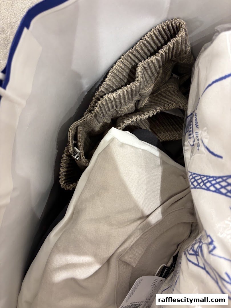A shopping bag filled with new clothes, including patterned trousers and a light-colored top.