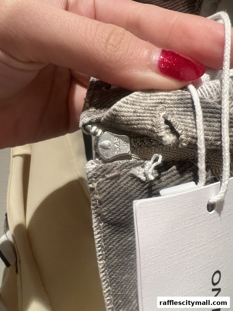 A close-up of a person's hand holding a garment with a zipper and tag from Urban Revivo.