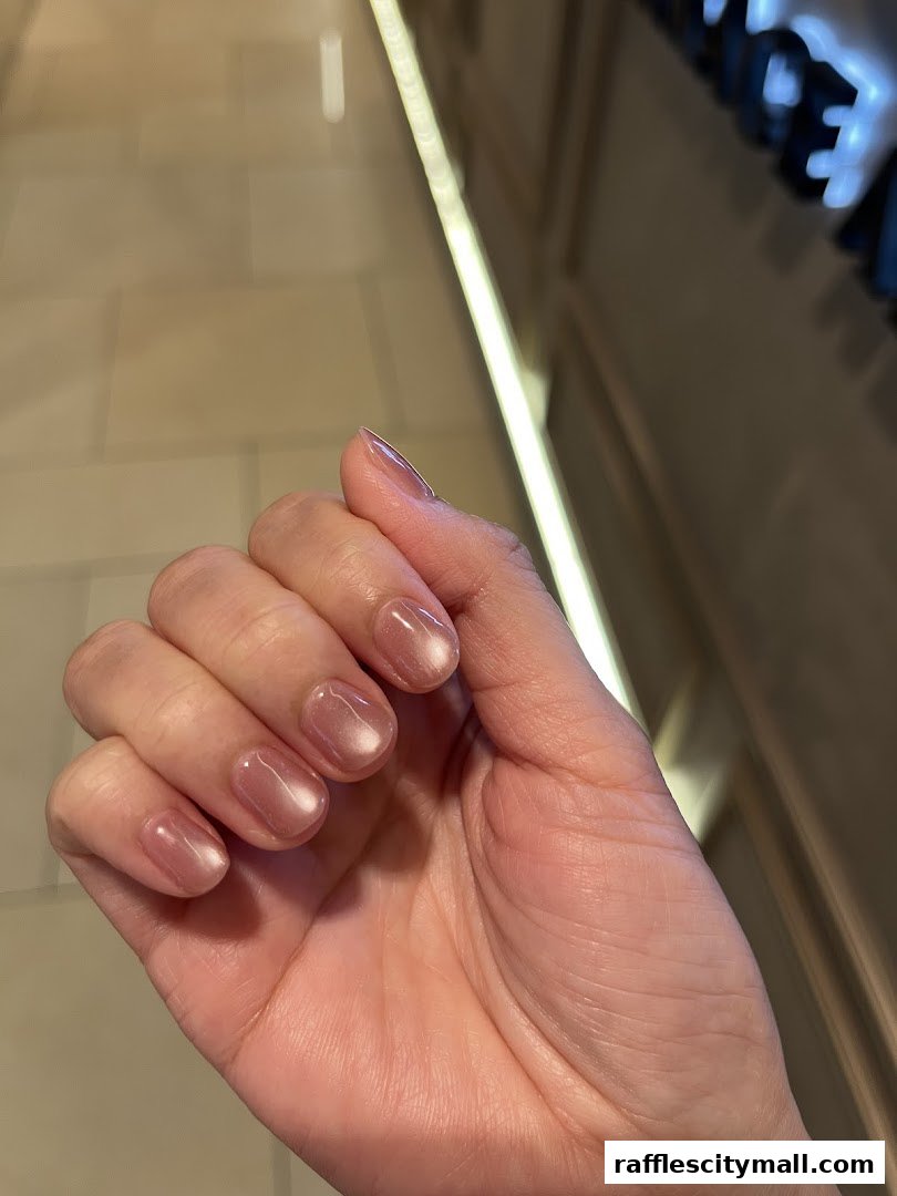 A close-up shot of a hand with perfectly manicured, shimmery nude nails.