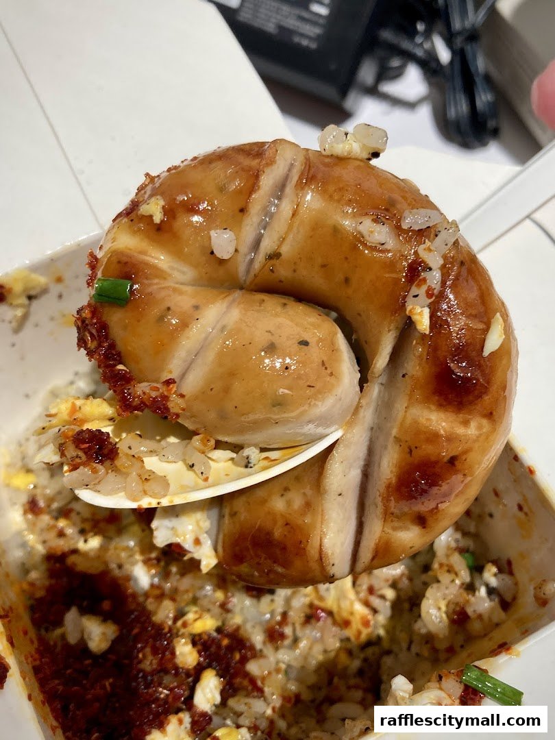 A close-up of a spoon lifting a glistening sausage over a bowl of fried rice.