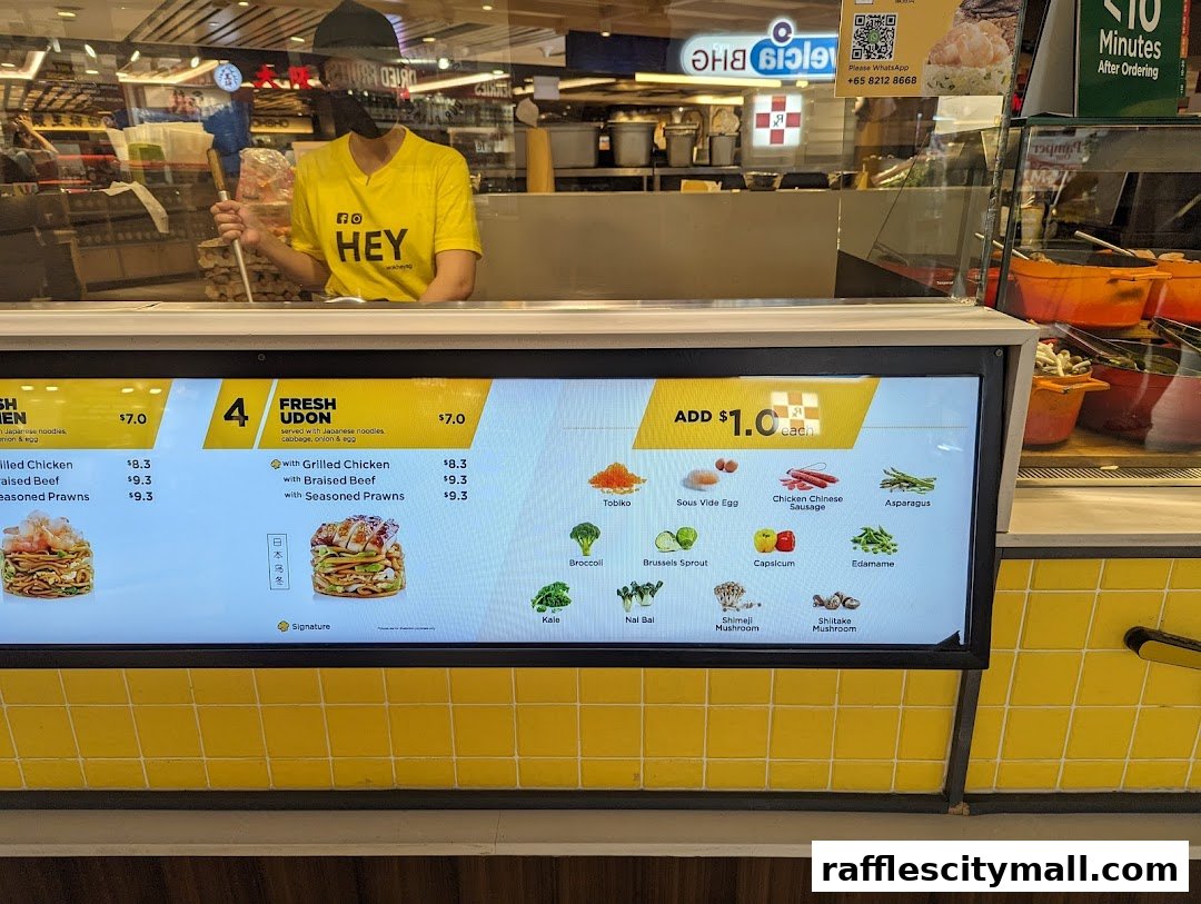 A digital menu board displaying noodle dishes and customizable toppings at Wok Hey.