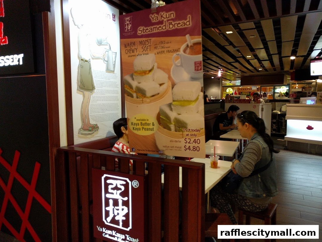 A display board for Ya Kun Kaya Toast featuring steamed bread and prices, with customers seated inside.
