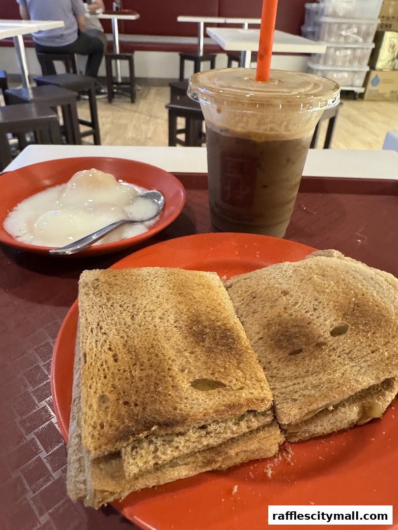 A close-up of a Ya Kun Kaya Toast meal featuring kaya toast, soft-boiled eggs, and a coffee drink.