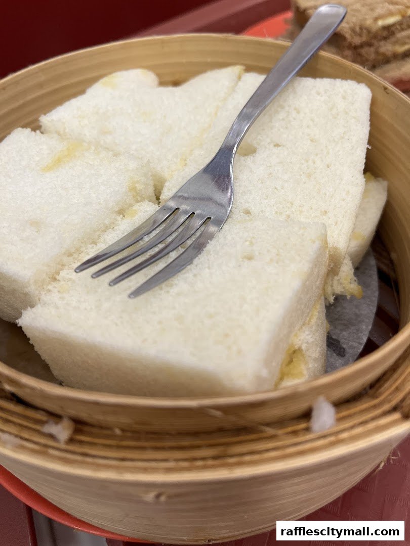A close-up of steamed white bread slices with kaya and a fork in a bamboo steamer.