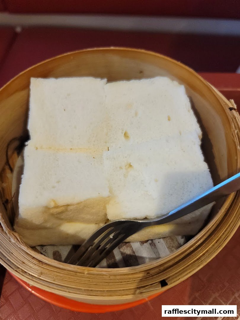A close-up of steamed kaya toast with a fork in a bamboo steamer.