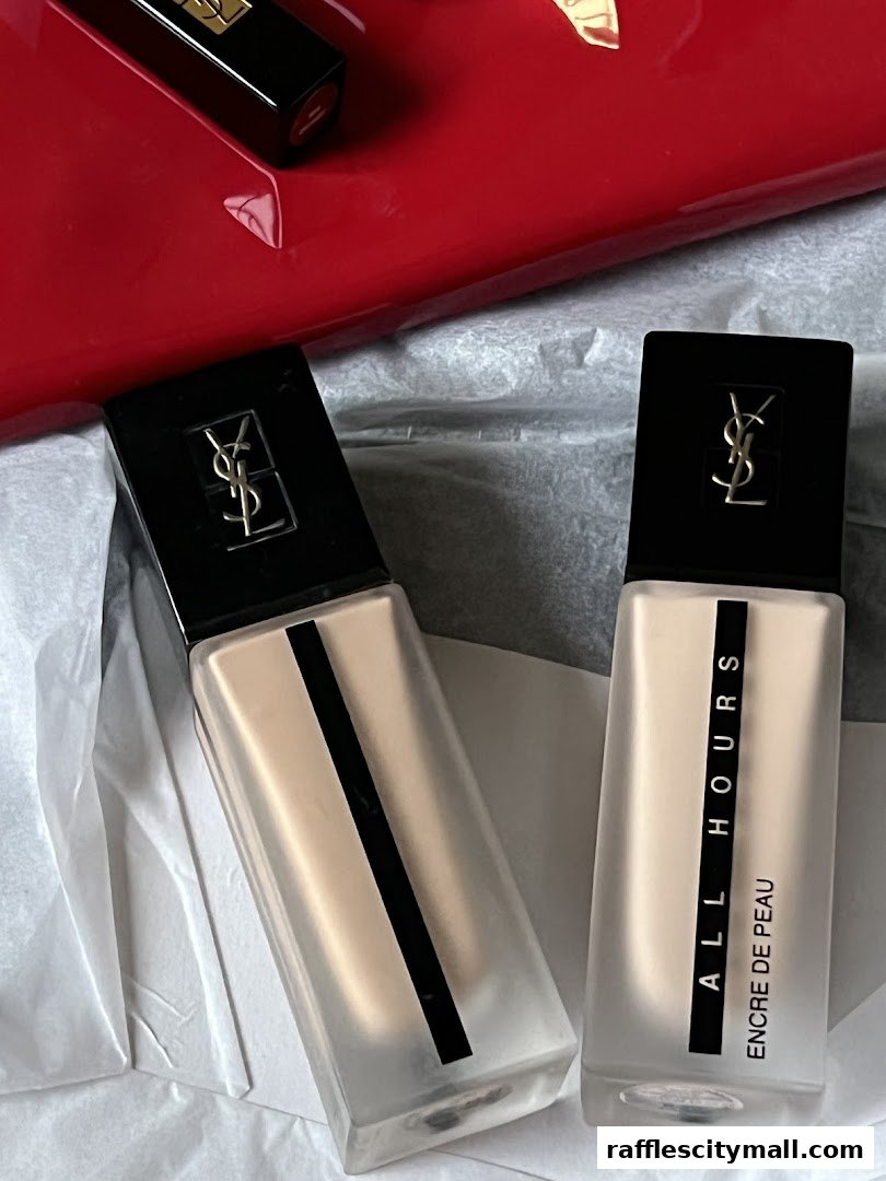 YSL Beauty foundation bottles and lipstick on a red surface with white tissue paper.